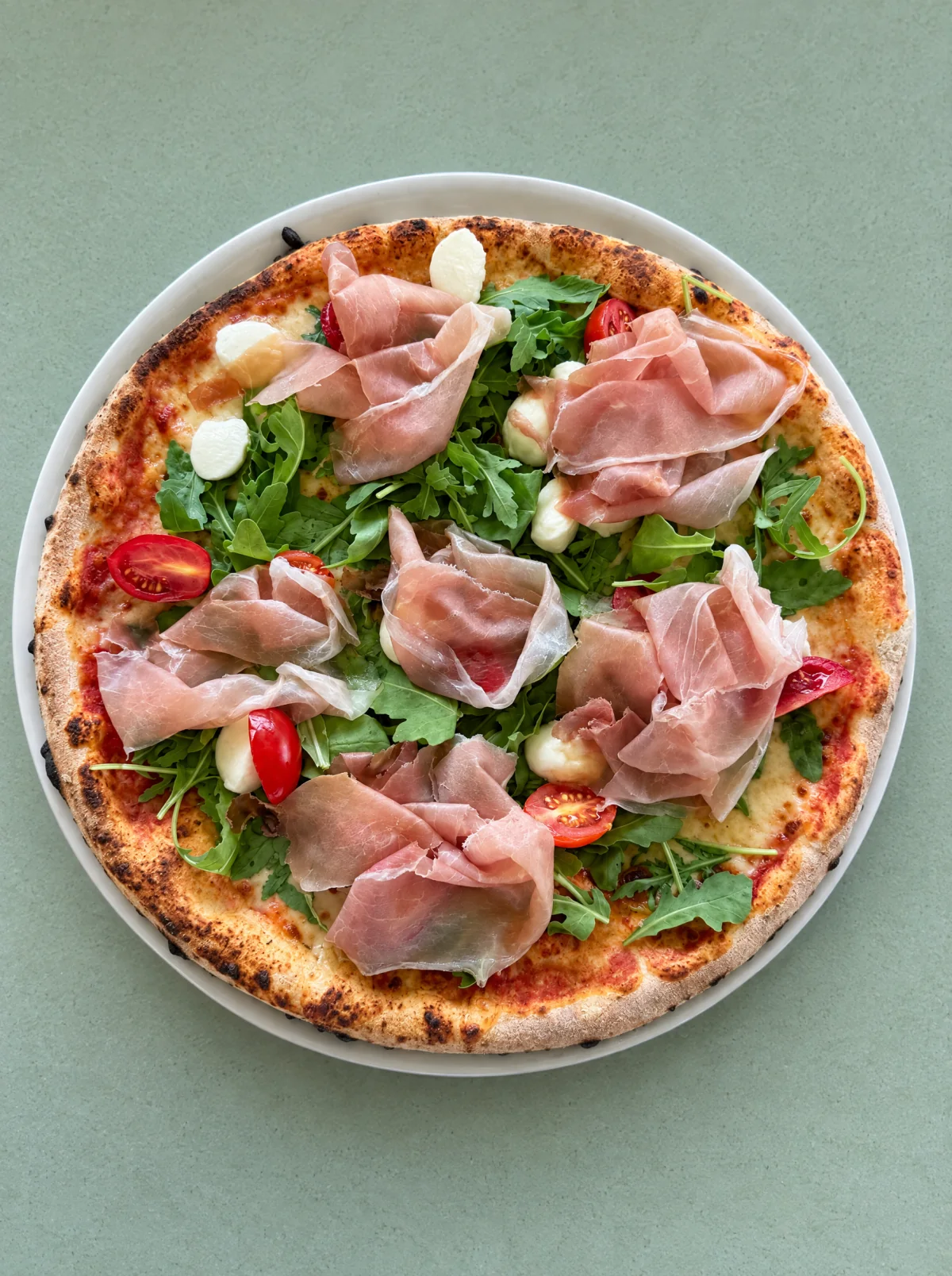 Pizza con prosciutto, rucola, pomodorini e mozzarella